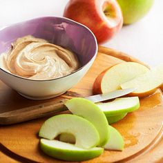 an apple and some sliced apples on a cutting board with peanut butter in a bowl