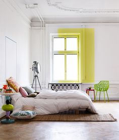 a bed sitting in a bedroom next to a green chair and yellow window on the wall