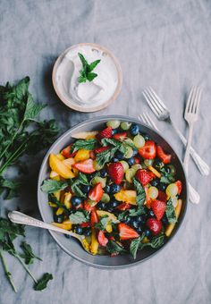 a bowl filled with fruit and vegetables next to a fork, knife and spoon on a table