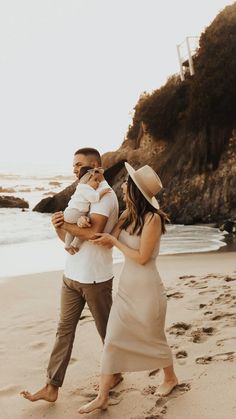 a man and woman walking on the beach with their baby in his arms while holding an infant