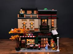 a lego model of a building with people on the front and second story windows, lights, and trees