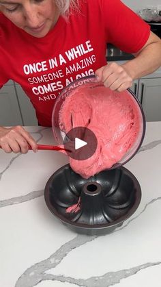 a woman in a red shirt is decorating a cake with pink icing on a white table