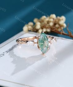 a ring with an oval cut green stone surrounded by small white diamonds on top of a card