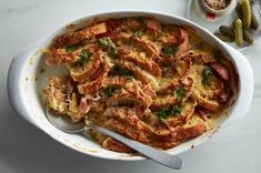 a casserole dish with meat and vegetables in it on a table next to pickles