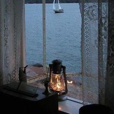 an open window overlooking the water with a sailboat in the distance and lights on