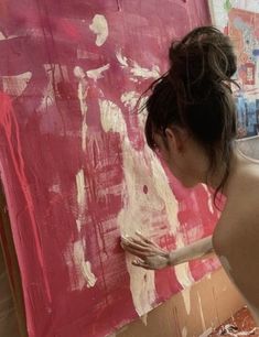 a woman is painting on the wall with pink and white paint