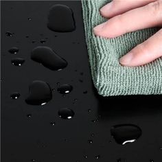 a person's hand on top of a black surface with water drops and a green cloth