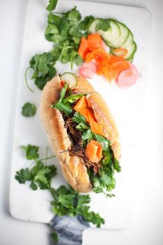 a sandwich with meat and vegetables on a cutting board next to cucumbers, tomatoes, and parsley