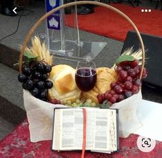 a basket filled with grapes, bread and wine next to an open book on a table