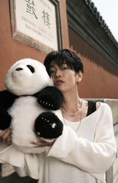 a woman holding a stuffed panda bear in front of a building