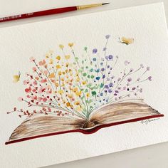 an open book painted with watercolors on white paper next to a red pencil