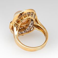 This radiant ring features an oval shaped gallery accented with one (1)  saltwater Akoya pearl, and a halo of twenty (20) bead set round brilliant cut diamond accents. The ring measures 21.6mm at the top, rises 10.7mm above the finger, tapering to 3.0mm wide and 1.0mm thick at the base of the shank.   It is crafted in 18k yellow gold and is currently a size 4.75.  The ring matches perfectly with the earrings under sku ab73326. Luxury Yellow Gold Pearl Ring With Round Cut, Akoya Pearl Ring, Radiant Ring, Saltwater Pearls, Pearl And Diamond Ring, Swirl Ring, Oval Face, Bead Set, Oval Faces