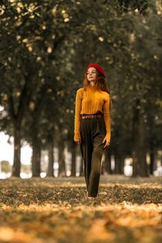 a woman with red hair is walking through the park wearing green pants and a yellow sweater