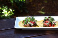 two tacos on a white plate sitting on a wooden table with green garnish