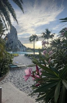 there is a large waterfall in the distance with pink flowers on the sand and palm trees around it