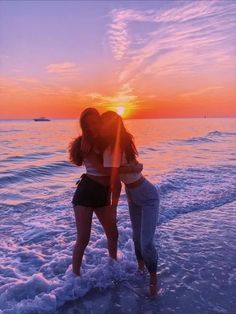 two girls are standing in the ocean at sunset