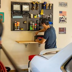 a man working on a workbench in a garage with tools hanging on the wall