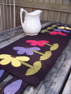 a white pitcher sitting on top of a wooden table next to a purple flower rug