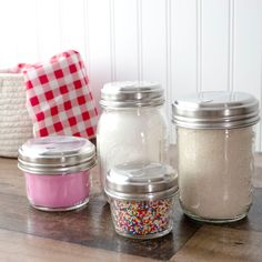 three glass jars filled with different colored sprinkles on top of a wooden table