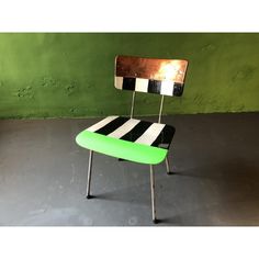 a green and black chair sitting on top of a cement floor next to a green wall