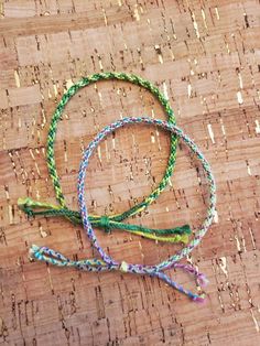 two bracelets are sitting on top of a piece of wood with beads and thread