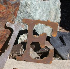 two rusty metal letters sitting next to each other on top of a stone slab with rocks in the background