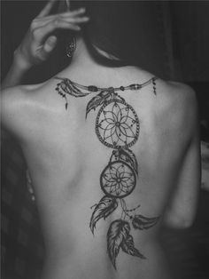 the back of a woman's body with a dream catcher tattoo on her lower back