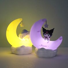 two small figurines sitting on top of a moon shaped night light, one with a cat and the other with a star