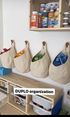 three canvas bags hanging on the wall next to shelves with bins and containers in them