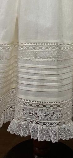 an image of a white curtain with lace on the bottom and bottom edge, in front of a wooden table