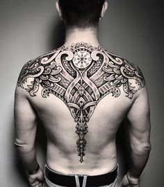 a man with a clock tattoo on his back is standing in front of a wall