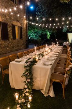 a long table is set up with candles and flowers for an outdoor dinner party in the evening