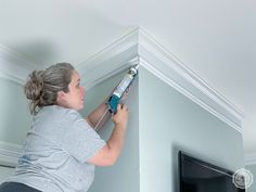 a woman is using a drill to paint the ceiling