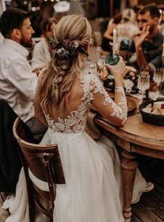 the back of a bride's dress sitting at a table with candles in front of her