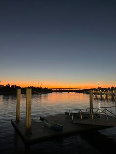 there is a boat dock on the water at sunset with a bridge in the background