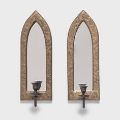 two decorative mirrors mounted to the side of a wall with candle holders on each one