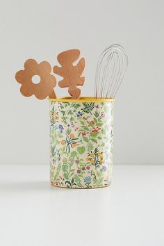 a flower pot with wooden utensils in it on a table next to a white wall