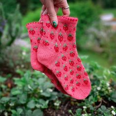 a woman's hand holding two pink socks in front of green plants and flowers