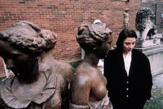 a woman standing next to some statues in front of a brick building