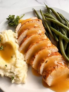 a white plate topped with meat, mashed potatoes and gravy next to green beans