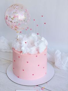 a pink cake with white frosting and hearts on top is topped with balloons in the shape of heart shapes