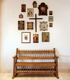 a wooden bench sitting in front of a wall covered with pictures and framed cross paintings