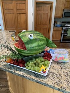 a fish made out of watermelon and grapes on a kitchen counter