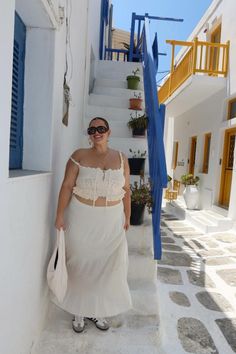 a woman in a white dress is walking down the street with her hands on her hips