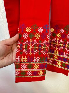 two red sweaters with snowflakes on them being held by someone's hand