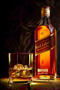 a bottle of red label whiskey next to a glass with ice cubes