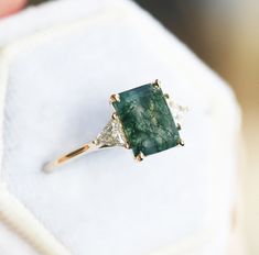 a green stone ring sitting on top of a white cloth covered cushioned surface with diamond accents