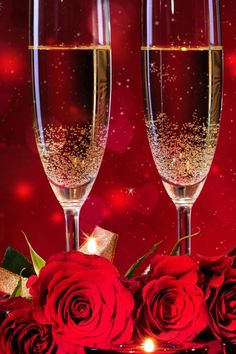 two glasses of champagne and roses on a red tablecloth with sparkling lights in the background