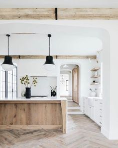 an open kitchen and dining room with white walls, wood flooring and black pendant lights