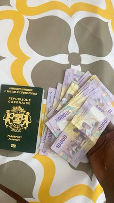 a person holding a passport and money in front of a yellow and white wallpaper